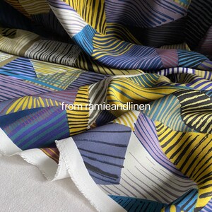 Peut inclure: Tissu géométrique abstrait avec des rayures jaunes, bleues, violettes et blanches. Le tissu est plié et a un bord blanc.