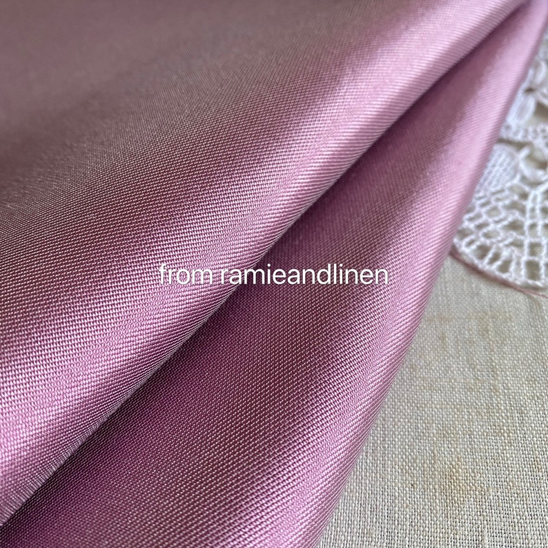 May include: Close-up of a smooth, silky fabric in a dusty rose color. The fabric is folded in half and has a subtle sheen.