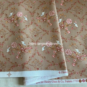Puede incluir: Una tela marrón con un patrón repetido de rosas rosas, pájaros blancos y enredaderas marrones. La tela tiene un borde blanco con el texto "Designs for Henry Glass & Co. Pattern 1733" impreso en ella.