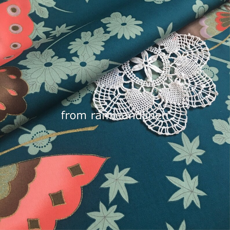 K&ouml;nnte beinhalten: Tealfarbener Stoff mit einem Blumenmuster und einem rosafarbenen Schmetterlingsdesign. Auf dem Stoff liegt eine wei&szlig;e H&auml;keldeckchen. Der Text "from ramieandlinen" ist im Bild sichtbar.