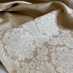 May include: A close-up of a beige fabric with a white damask pattern. The fabric is soft and luxurious, and it would be perfect for upholstery or curtains.