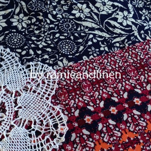 Pu&ograve; includere: Un centrino bianco all'uncinetto con un motivo floreale, posto su un tessuto a motivi rossi e blu con il testo "by ramieandlinen".