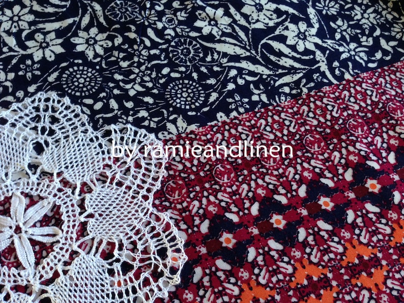 Pu&ograve; includere: Un centrino bianco all'uncinetto con un motivo floreale, posto su un tessuto a motivi rossi e blu con il testo "by ramieandlinen".