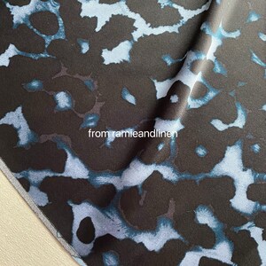 May include: Close-up of a dark blue fabric with a light blue abstract pattern. The fabric has a soft, silky texture. "from ramieandlinen" is printed on the fabric.