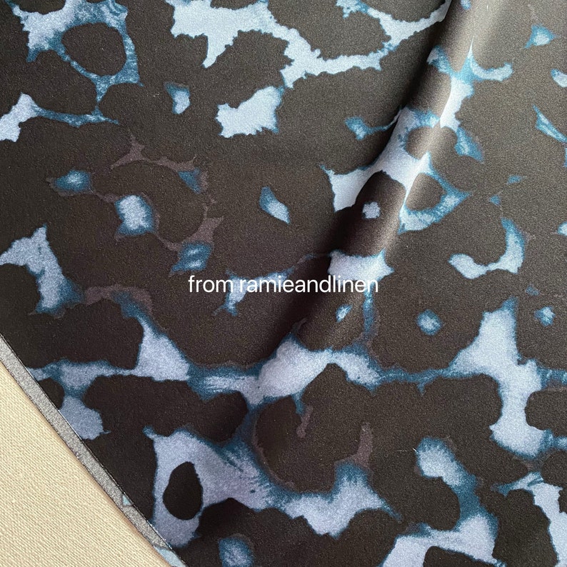 May include: Close-up of a dark blue fabric with a light blue abstract pattern. The fabric has a soft, silky texture. "from ramieandlinen" is printed on the fabric.