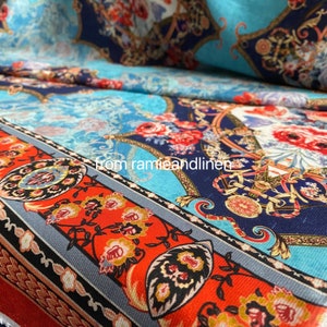 May include: A close-up of a colorful fabric with a blue, red, and gold patterned design. The fabric features a repeating pattern of flowers, swirls, and geometric shapes.