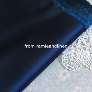 May include: A close-up of a dark blue satin fabric with a fringed edge. The fabric is lying on a white surface with a lace doily. The text "from ramieandlinen" is visible in the image.