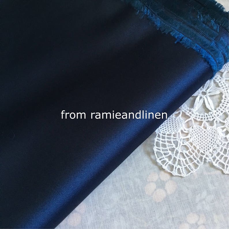 May include: A close-up of a dark blue satin fabric with a fringed edge. The fabric is lying on a white surface with a lace doily. The text "from ramieandlinen" is visible in the image.