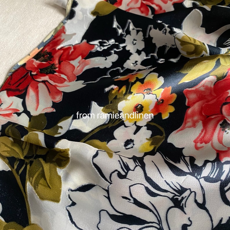 May include: Close-up of a black and white floral fabric with red, yellow, and green accents. The fabric has a silky sheen and a soft drape.