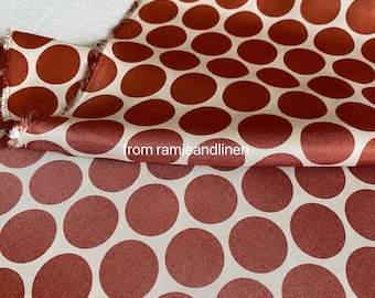 May include: Close-up of a rust-colored fabric with large white polka dots. The fabric is folded in half, showing the pattern on both sides.