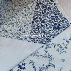 May include: Two pieces of white fabric with a blue floral pattern. The fabric is folded in half, with the patterned side facing out. The fabric is from the company "from jamieandlinen".