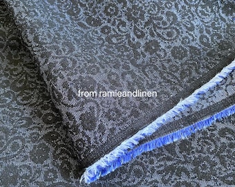 May include: Close-up of a dark blue fabric with a floral paisley pattern. The fabric has a textured appearance and a frayed edge with blue fringe. The text "from ramieandlinen" is visible.