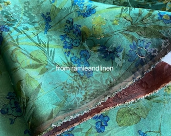 May include: A close-up of a teal fabric with a floral pattern. The design features blue and green flowers and foliage. The text "from ramieandlinen" is visible on the fabric.
