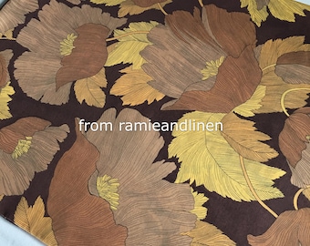 Op de afbeelding: Bruine stof met een bloemenpatroon met grote, gestileerde bloemen in tinten bruin, beige en geel op een donkerbruine achtergrond. De stof heeft een textuur, bijna als linnen.