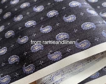 May include: Close-up of a dark blue fabric with a white and blue paisley pattern. The fabric has a white border and is folded over.
