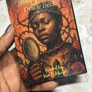 May include: A box for the "Shadow Sisters Oracle Deck" with an illustration of a person wearing a crown of thorns and holding a mirror. The artwork uses warm colours, roses, and the text "Created By Vera L Johnson".