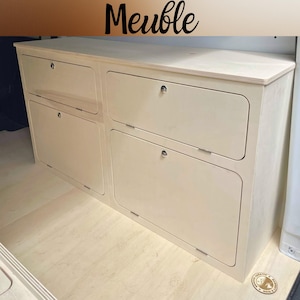 Può includere: Un mobile contenitore in legno chiaro con quattro ante rettangolari dagli angoli arrotondati e serrature color argento. L'unità presenta una superficie superiore piatta e una finitura liscia. La parola Meuble è stampata in nero in alto.