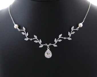 May include: A silver necklace with a delicate vine design and a teardrop-shaped crystal pendant. The necklace is accented with two small pearl beads.