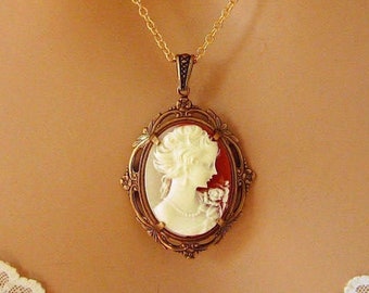 May include: A gold chain necklace with a cameo pendant. The cameo features a white profile of a woman with a red background.