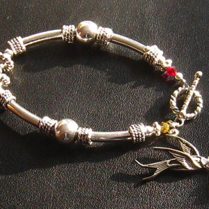 May include: A silver bracelet with a silver bird charm, red and yellow beads, and a toggle clasp.