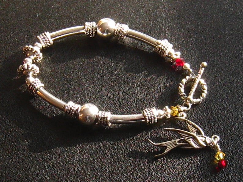 May include: A silver bracelet with a silver bird charm, red and yellow beads, and a toggle clasp.