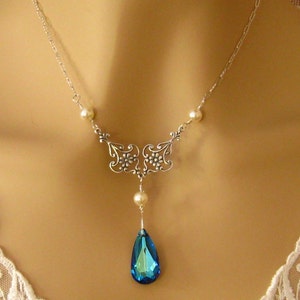 May include: A silver necklace with a blue teardrop pendant and pearl accents. The necklace features a delicate floral design.