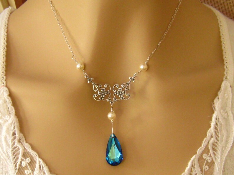 May include: A silver necklace with a blue teardrop pendant and pearl accents. The necklace features a delicate floral design.