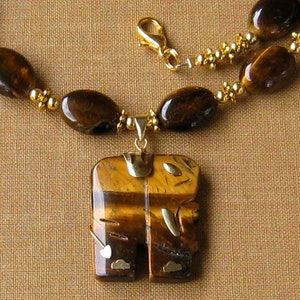 May include: A gold necklace with a large tiger's eye pendant. The pendant is carved in the shape of a stylised figure. The necklace is made of tiger's eye beads and gold beads.