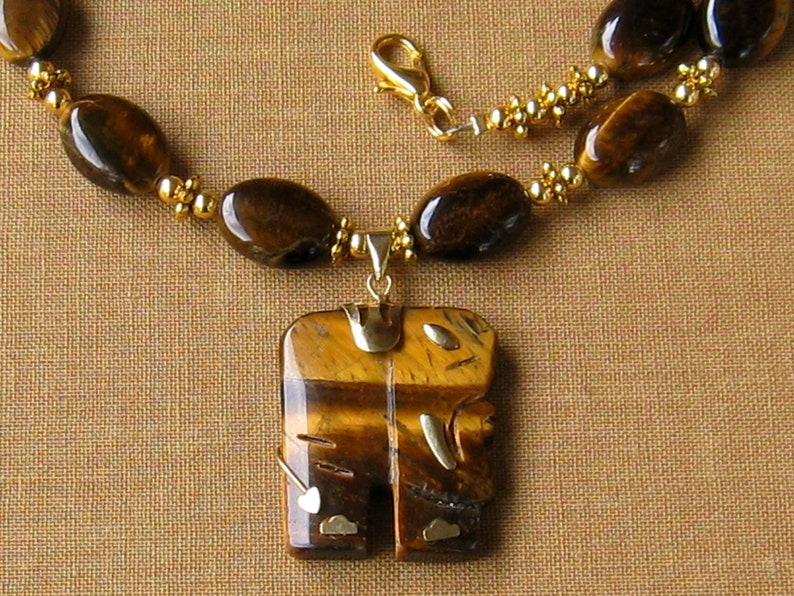 May include: A gold necklace with a large tiger's eye pendant. The pendant is carved in the shape of a stylised figure. The necklace is made of tiger's eye beads and gold beads.