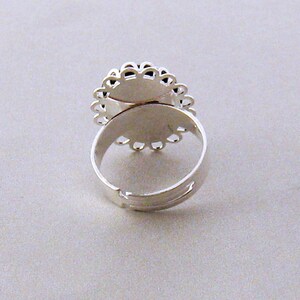 May include: Silver ring with a round, open-backed setting. The setting has a delicate, scalloped edge.
