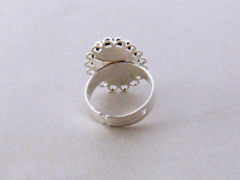 May include: Silver ring with a round, open-backed setting. The setting has a delicate, scalloped edge.
