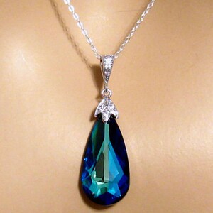 May include: A silver chain necklace with a teardrop-shaped pendant. The pendant is a large, faceted, blue crystal with a green hue.