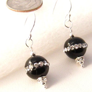 May include: Black bead earrings with silver hooks and a row of clear rhinestones around the bead.