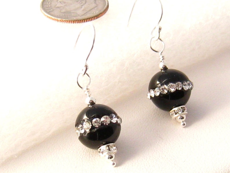 May include: Black bead earrings with silver hooks and a row of clear rhinestones around the bead.