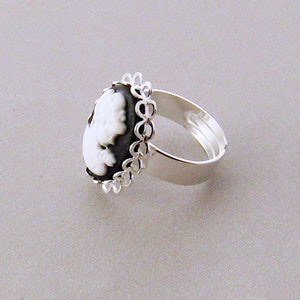 May include: A silver ring with a black and white cameo featuring a woman's profile. The cameo is surrounded by a delicate silver filigree design.