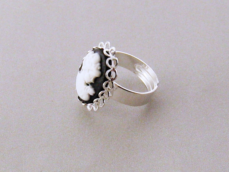 May include: A silver ring with a black and white cameo featuring a woman's profile. The cameo is surrounded by a delicate silver filigree design.