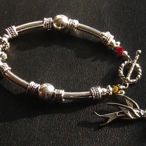 May include: Silver bracelet with a silver bird charm, red and yellow beads, and a toggle clasp.