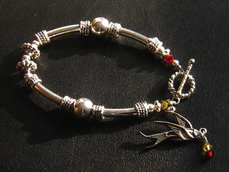 May include: Silver bracelet with a silver bird charm, red and yellow beads, and a toggle clasp.