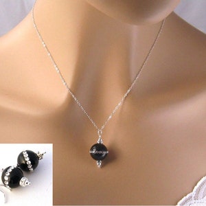 May include: A black onyx necklace and earrings set with a silver chain and small clear rhinestones. The necklace features a single round black onyx pendant with a silver accent.
