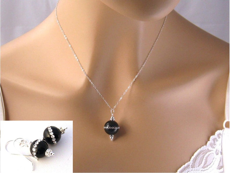 May include: A black onyx necklace and earrings set with a silver chain and small clear rhinestones. The necklace features a single round black onyx pendant with a silver accent.