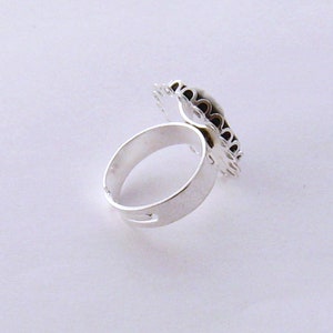 May include: A silver ring with a decorative design on the top. The design is made of small, intricate details and appears to be a floral pattern.