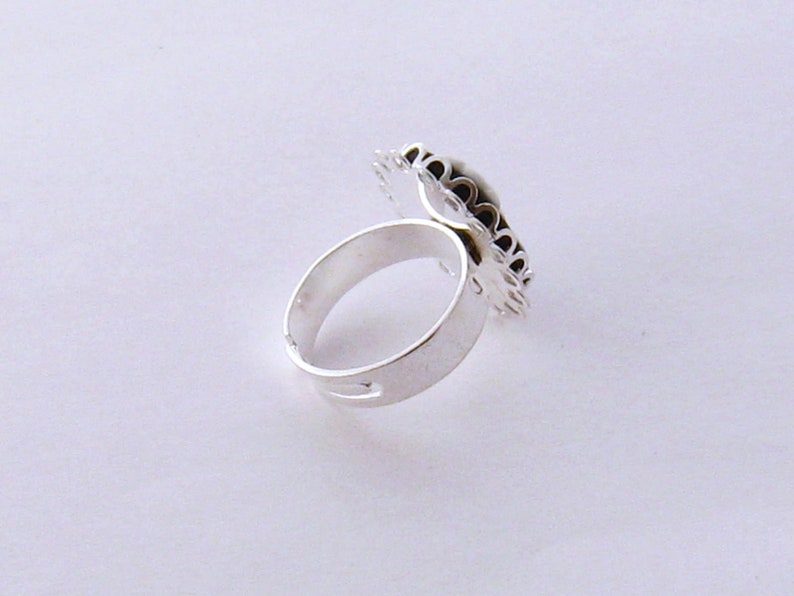 May include: A silver ring with a decorative design on the top. The design is made of small, intricate details and appears to be a floral pattern.