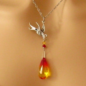 May include: A silver-toned necklace featuring a detailed swallow pendant. The pendant suspends a teardrop-shaped crystal with a gradient of red to yellow. Small red and yellow beads accent the design, creating a striking jewelry piece.