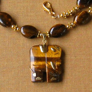 May include: A gold necklace with a tiger's eye pendant in the shape of an elephant. The pendant has gold accents and the necklace is made of tiger's eye beads.