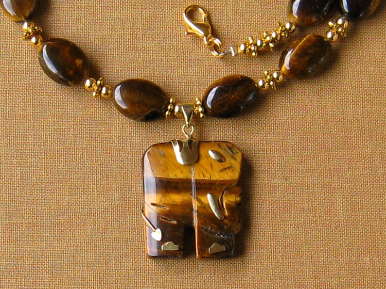 May include: A gold necklace with a tiger's eye pendant in the shape of an elephant. The pendant has gold accents and the necklace is made of tiger's eye beads.