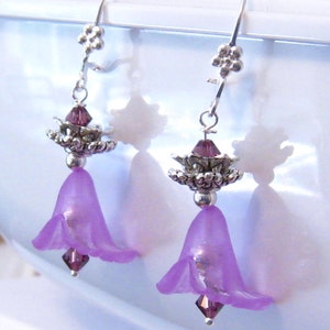 Pode incluir: Brincos pendentes de flor roxa com detalhes prateados e contas de cristal.