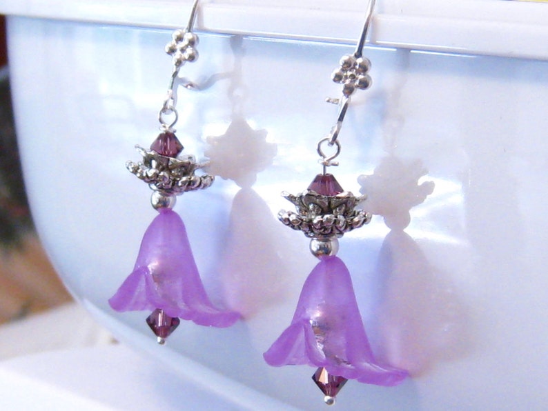 Pode incluir: Brincos pendentes de flor roxa com detalhes prateados e contas de cristal.