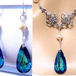 May include: A silver necklace with a teardrop-shaped blue and green crystal pendant and a pearl accent. Matching earrings with blue and green crystal teardrop pendants and pearl accents.