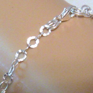 May include: A silver chain bracelet with a textured, oval-shaped link design. The bracelet has a lobster claw clasp.