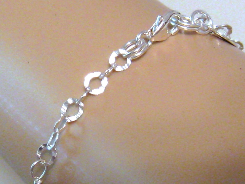 May include: A silver chain bracelet with a textured, oval-shaped link design. The bracelet has a lobster claw clasp.